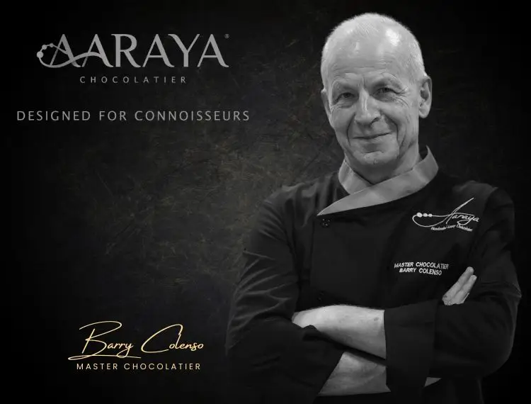 Barry Colenso, world-renowned Master Chocolatier for AARAYA®, wearing a black chef’s coat with arms crossed, standing confidently against a dark textured background – expert behind AARAYA®'s luxury handcrafted chocolate creations.