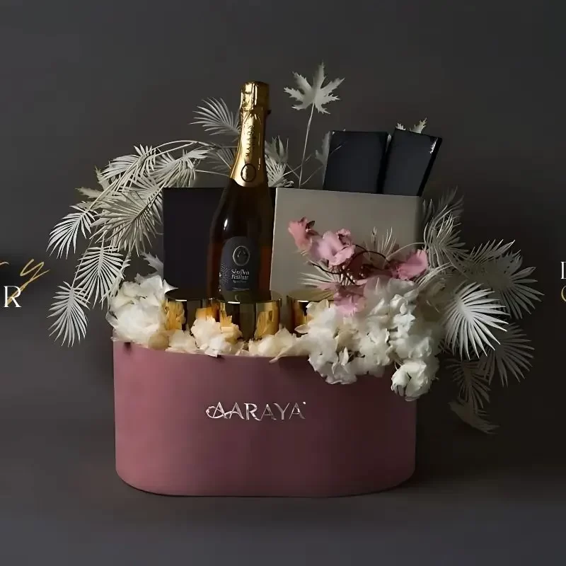 Luxury pink floral hamper by AARAYA® featuring a sparkling beverage, premium gift boxes, gold cups, and elegant white and pink floral arrangement – ideal for gifting in Dubai.