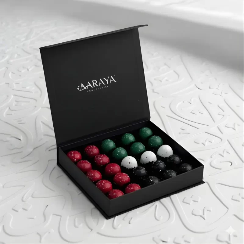 Luxury black compact gift box by AARAYA® containing 25 artisanal chocolates arranged in UAE National Day colours.