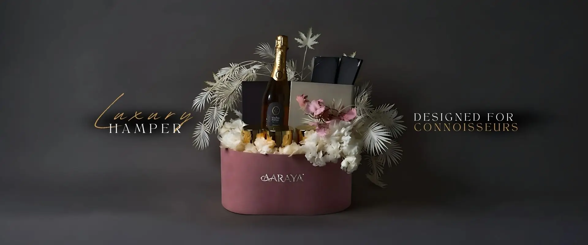 Luxury pink floral hamper by AARAYA® featuring a sparkling beverage, premium gift boxes, gold cups, and elegant white and pink floral arrangement – ideal for gifting in Dubai.